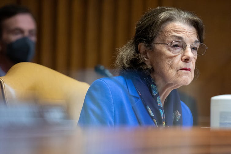 An older woman with black hair looking out from a desk.