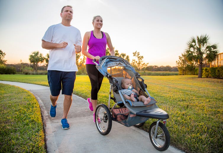 A couple go for an evening walk in a park. The woman pushes a stroller with her baby.