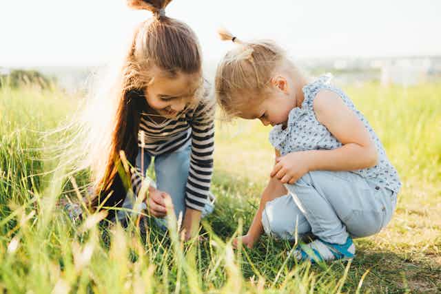 Two young girls looking at something small in grass field