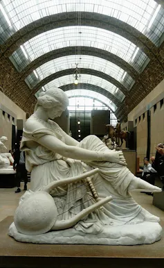 Estatua de una mujer con las piernas cruzadas mirando al suelo.