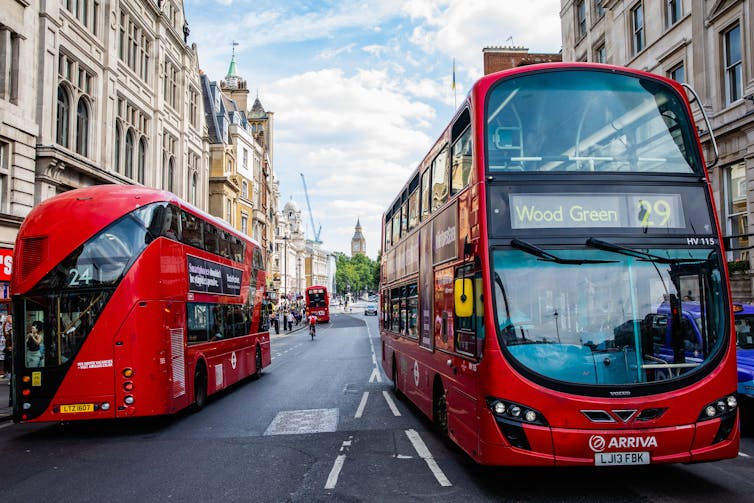 Two red double-decker buses pass each other along Whitehall in central London.