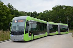 A green bus with several segments connected by flexible panels.