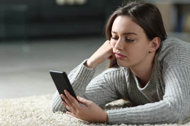 A woman looks at a smartphone with a bored expression.