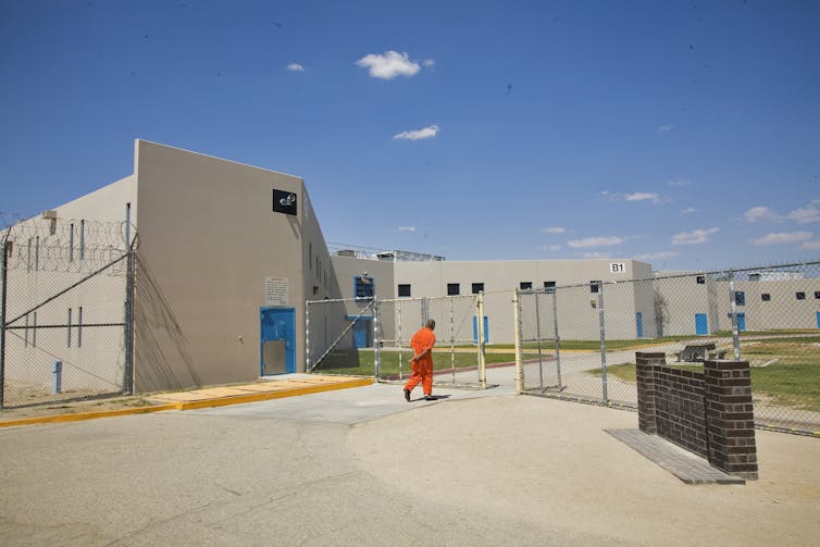 A person wearing a bright orange outfit is seen walking into gates towards a beige building.