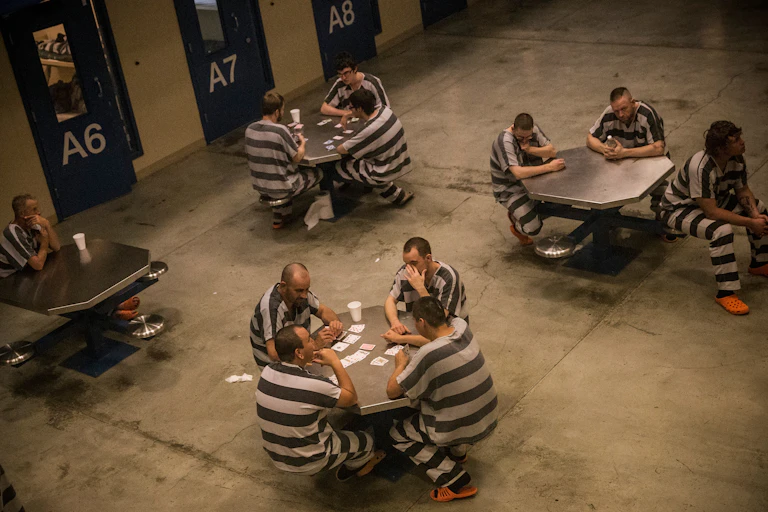People wearing white and black striped outfits sit around tables together in a barren room.