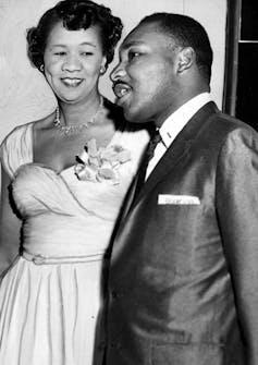 A woman in an evening dress with a corsage stands next to a man in a suit, both smiling and chatting.