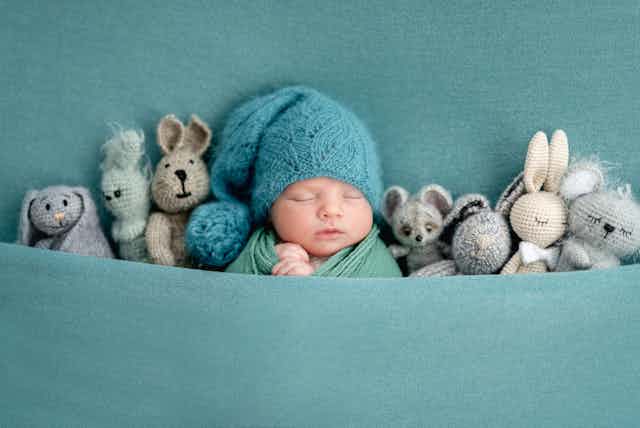 baby in beanie sleeping next to toys