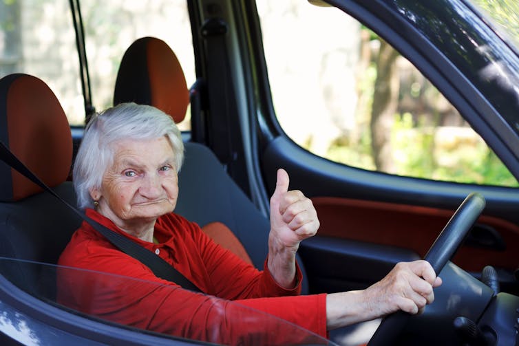 Elderly woman behind the wheel of a car gives a thumbs-up