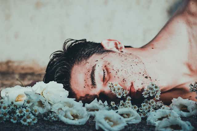 Sad boy with dirt on his face lying on the ground, near flowers, eyes closed