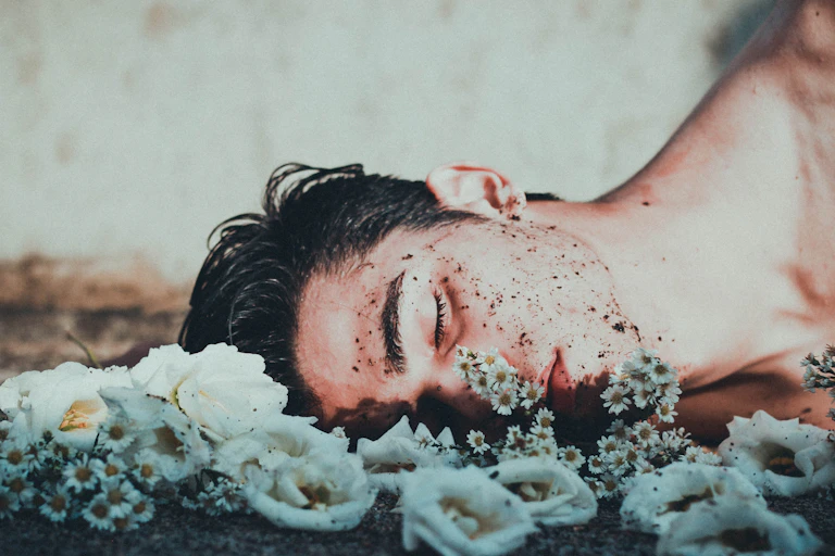 Sad boy with dirt on his face lying on the ground, near flowers, eyes closed