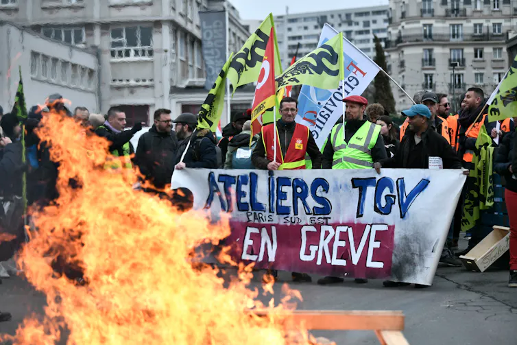 Des travailleurs des transports tiennent une banderole sur laquelle on peut lire « Atelier TGV Paris Sud-Est en grève » lors d’une manifestation à l’appel des syndicats français devant la gare de Lyon, à Paris, le 19 janvier 2023. Une journée de grèves et d