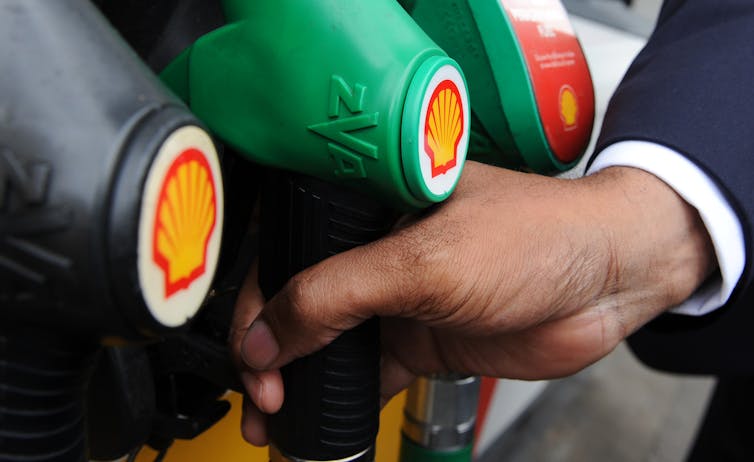A hand grasps a green petrol pump with Shell's logo on it.