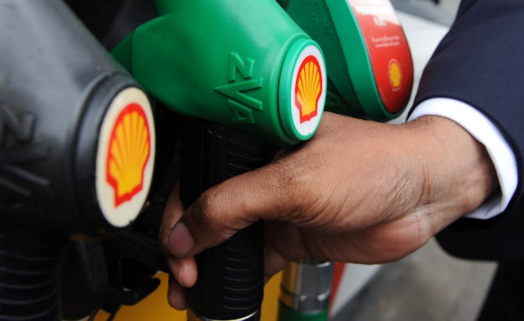 Uma mão segura uma bomba de gasolina verde com o logotipo da Shell.