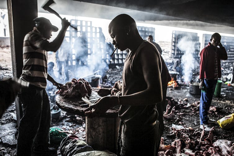 Several men chop and handle meat on makeshift tables, animal parts strewn on the floor.