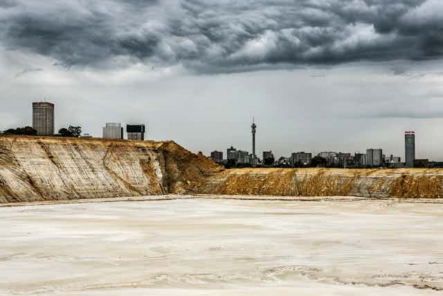 An abandoned mine dump with the skyline of a city behind it, dark clouds overhead.
