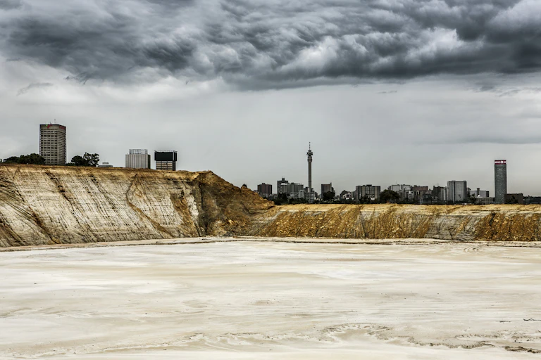 An abandoned mine dump with the skyline of a city behind it, dark clouds overhead.