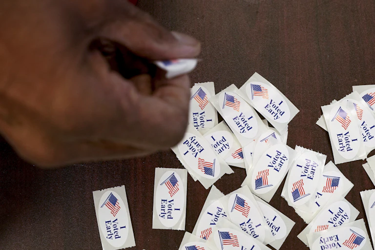 A Black hand picks up an 'I voted early' sticker.