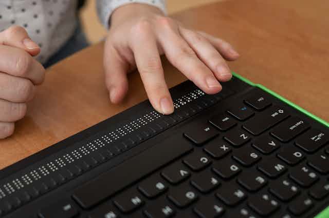 una mano toca un teclado de ordenador con una zona de teclado  Braille.