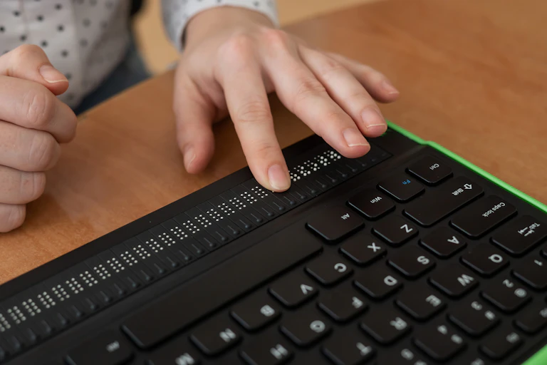 una mano toca un teclado de ordenador con una zona de teclado Braille.