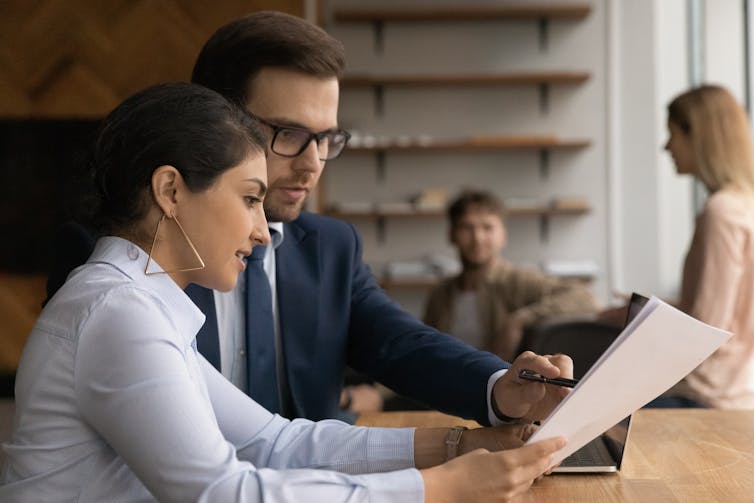 A young man and woman in professional clothing look at a paper document together and discuss