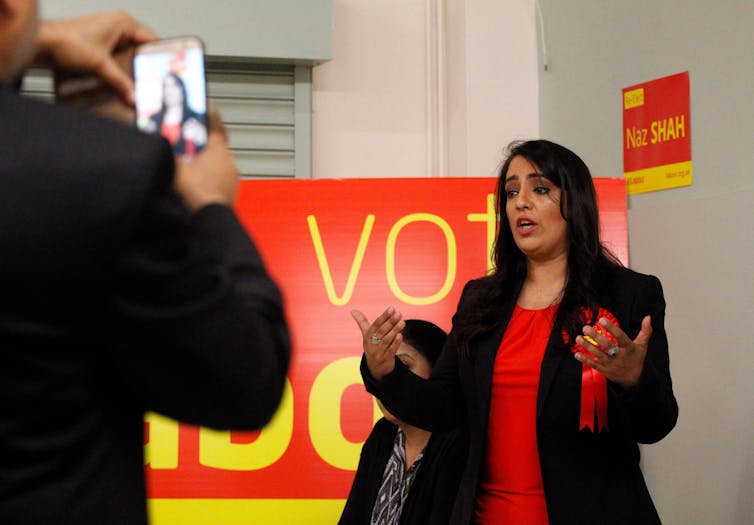 Naz Shah speaking in front of a Vote Labour sign.