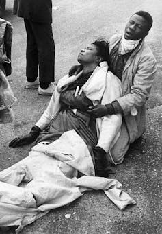 A man crouching on the pavement cradles an injured woman.