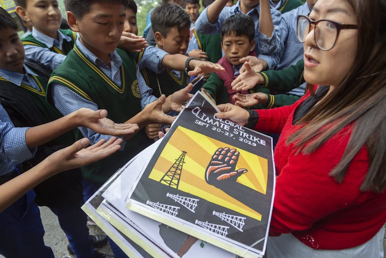 An adult seen bending over a climate poster surrounded by children.