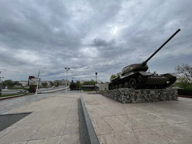 A tank is seen on an empty street with grey clouds. 