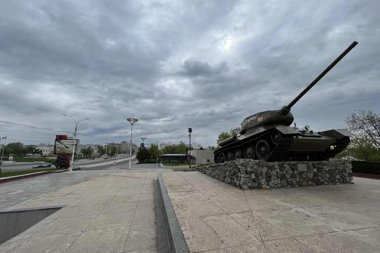 A tank is seen on an empty street with grey clouds.