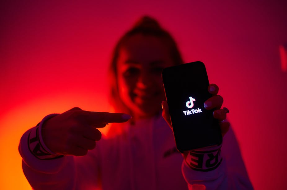 Jeune fille tenant un smartphone sur lequel s'affiche le logo de TiikTok