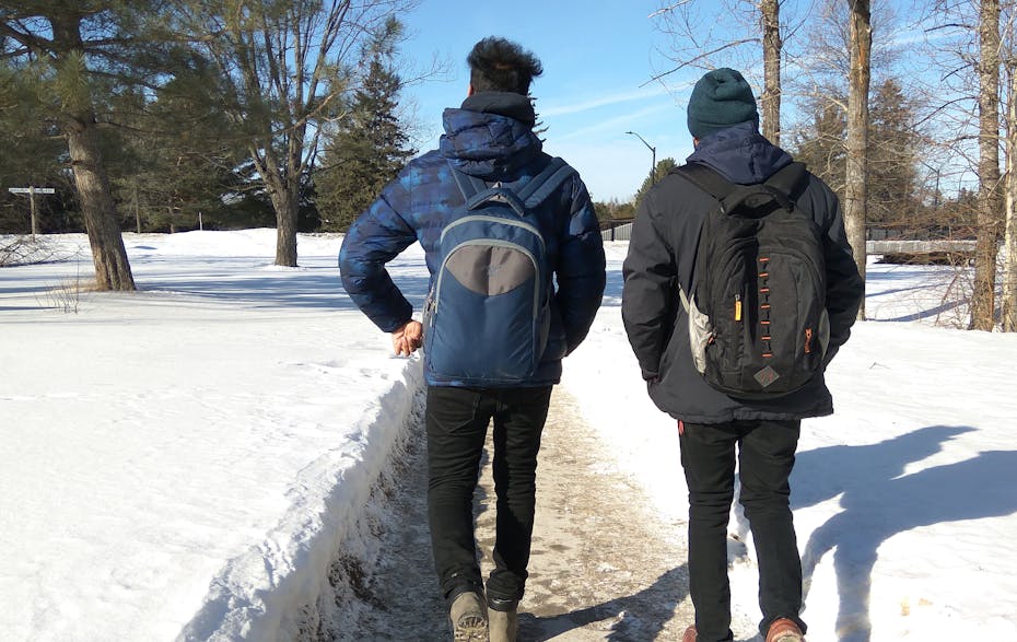 Two students seen walking in a snowy landscape on a campus.