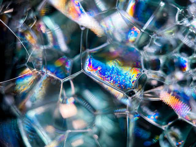 Iridescent colours shimmer on web of soap bubbles.