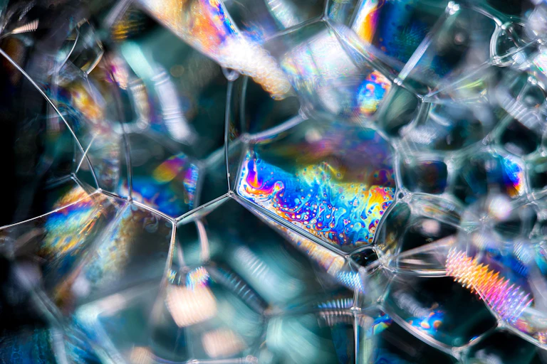 Iridescent colours shimmer on web of soap bubbles.