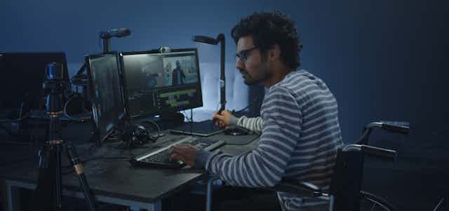 A man in a wheelchair sits at computers editing a film.