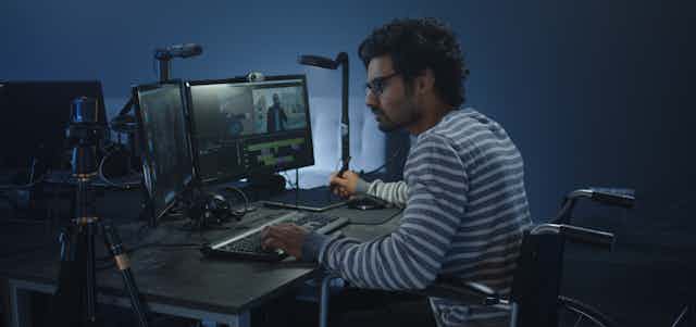 A man in a wheelchair sits at computers editing a film. 