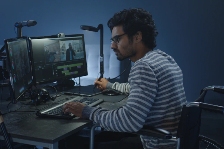A man in a wheelchair sits at computers editing a film.