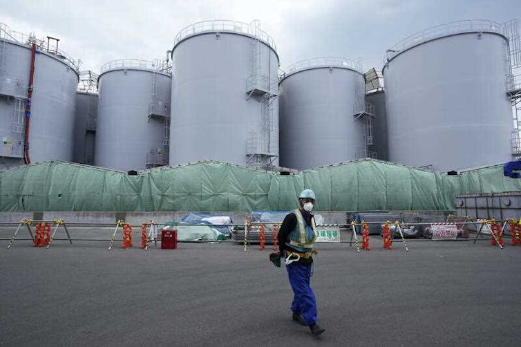 A worker helps direct a truck driver as he stands near tanks used to store treated radioactive water after it was used to cool down melted fuel at the Fukushima Daiichi nuclear power plant.