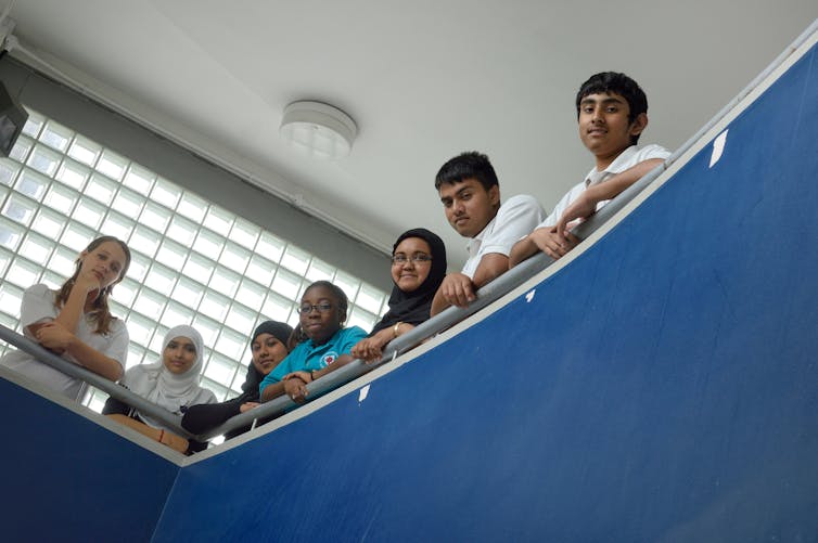 Teenagers seen from below, looking down from a balustrade.