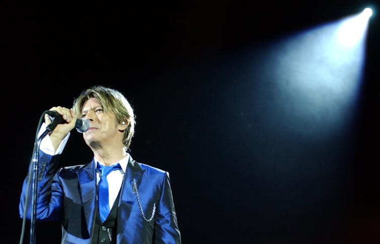 David Bowie in a blue suit with a microphone.