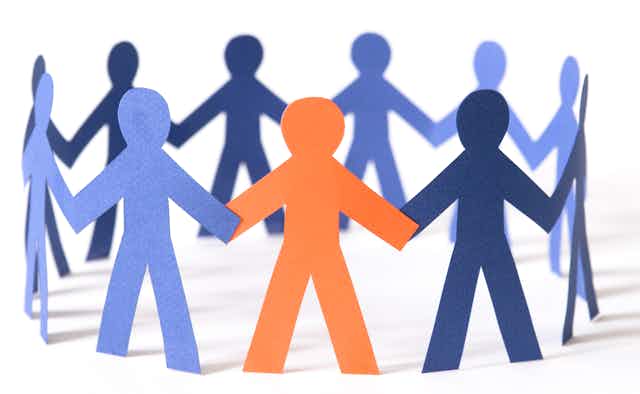 paper cutouts of people are pictured in a circle holding hands. most are blue, one is orange