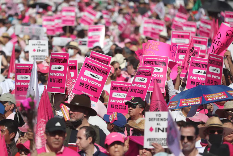 Protesters holding up pink and white placards rejecting reform to the National Electoral Institute (INE)