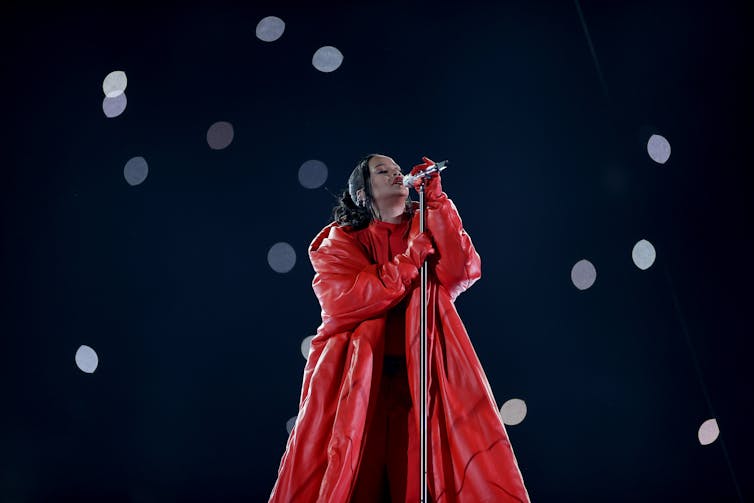 Rihanna performs in a large oversized red puffer coat, against a black backdrop