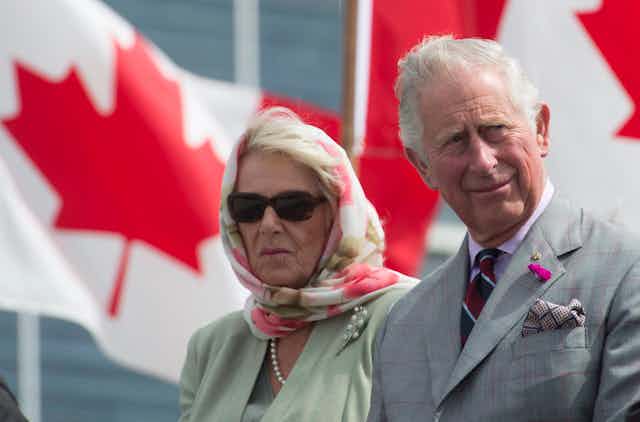 Charles and Camilla sit in front of Canadian flags.