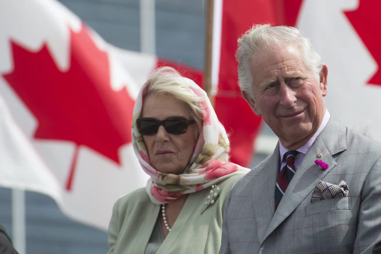 Charles and Camilla sit in front of Canadian flags.