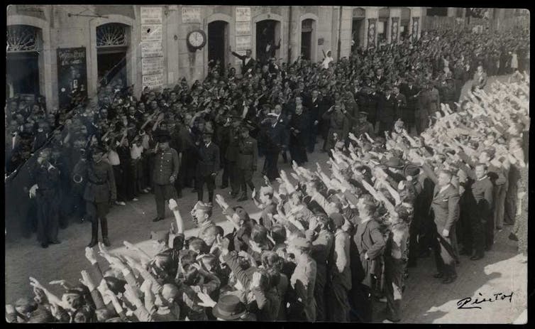 Civiles y militares hacen el saludo falangista al paso de una comitiva de despedida.