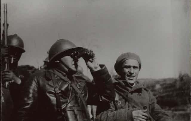 Un soldado mira con prismáticos en la lejanía mientras otro mira a cámara.