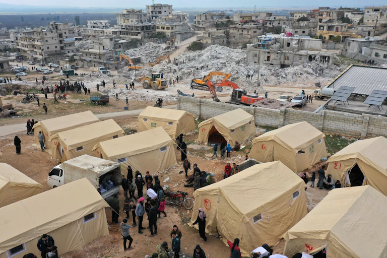 A dozen tents are set up near piles of rubble.
