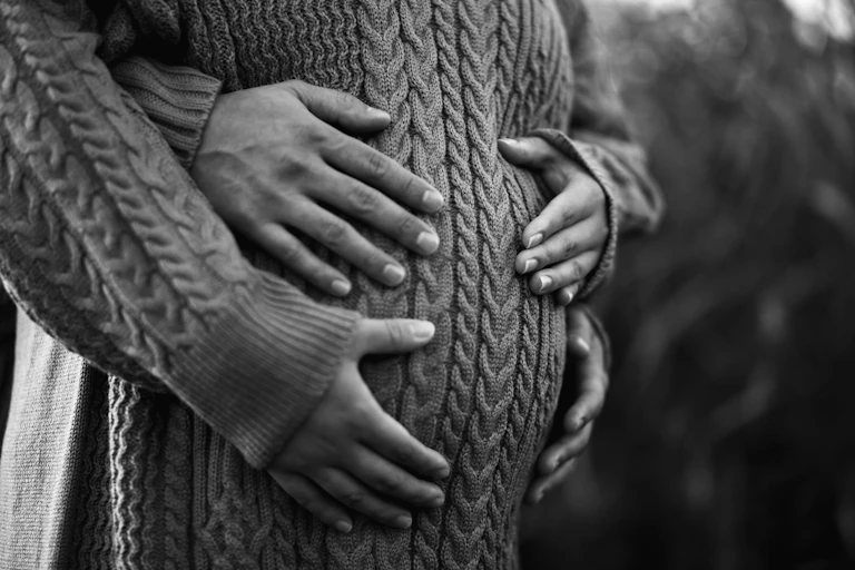 A pregnant woman's abdomen with her own hands and another person's hands on her belly