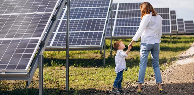Mother and son stand next to rows of solar panels