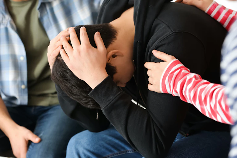 Dos personas consuelan a un joven con la cabeza entre las manos.